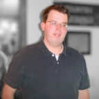 A white man with short cropped brown hair wearing perscription glasses.